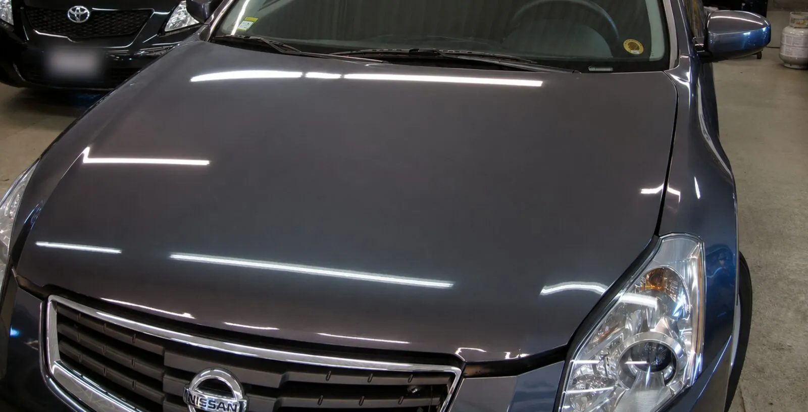 The same bonnet after paintless repair: the workshop lights reflect as clean, straight lines.